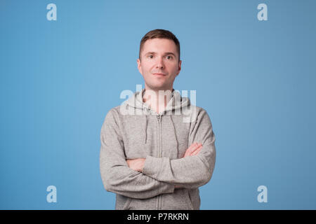 Confident young handsome man keeping arms crossed and smiling while standing against blue white background Stock Photo