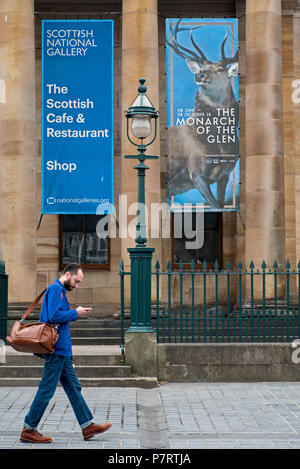 A visitor walking by the entrance to the National Gallery of Scotland at the Mound in Edinburgh with an advert out front for the Monarch Of The Glen. Stock Photo