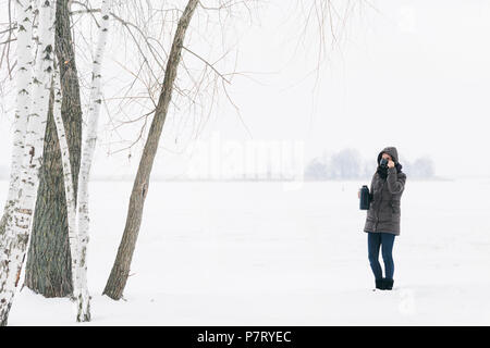Woman winter clothing standing snowy landscape drinks coffee from thermos Stock Photo