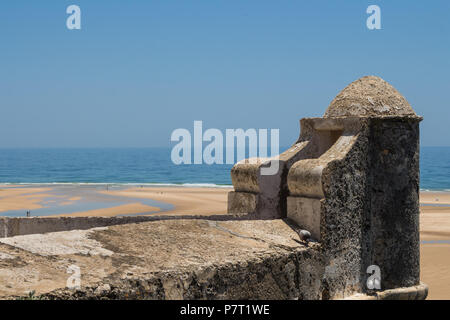 Tower of the old fortress made of stone. View on a sandy beach with puddles after a high tide. Horizon of the Atlantic ocean. Blue sky. Cacela Velha,  Stock Photo