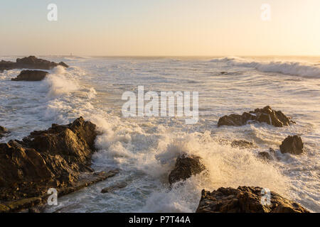 Stormy waves crashing over rocky coast at sunset Stock Photo