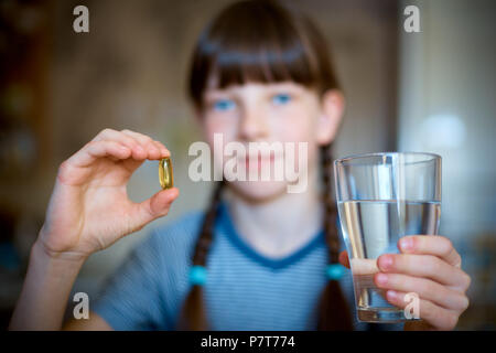 Capsules, pills in one hand, a glass of water in the other. The girl is holding the medicine in front of her. Close-up. Stock Photo