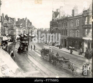 English: Broad Street, Reading, looking eastwards from an upper storey window, c. 1904. A tramcar heads eastwards, and two horse-drawn cabs wait in the middle of the road, by the trolley-pole. North side: No. 17 (W. and R. Fletcher, butchers); No. 14 (Royal Oak Inn); No. 6 (United Counties Bank). South side: Nos. 116 and 117 (Fergusons Ltd., Angel Brewery and Wine and Spirit Stores); Nos. 114 and 115 (Berkshire Training College of Music on the upper floors). 1900-1909. 1904 55 Broad Street, Reading, looking eastwards, c. 1904 Stock Photo