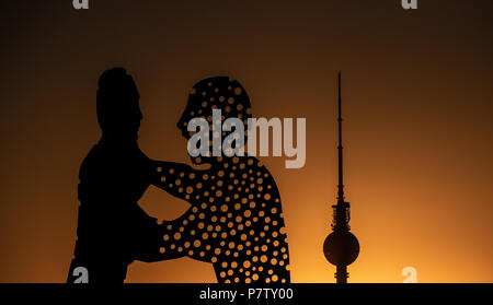 Berlin, Germany. 02nd July, 2018. The large sculpture Molecule Man by American artist Jonathan Borofsky glows orange in the sunset. Behind the sculpture looms Berlin's Television Tower. Credit: Paul Zinken/dpa/Alamy Live News Stock Photo