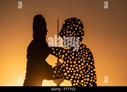 Berlin, Germany. 02nd July, 2018. The large sculpture Molecule Man by American artist Jonathan Borofsky glows orange in the sunset. Behind the sculpture looms Berlin's Television Tower. Credit: Paul Zinken/dpa/Alamy Live News Stock Photo