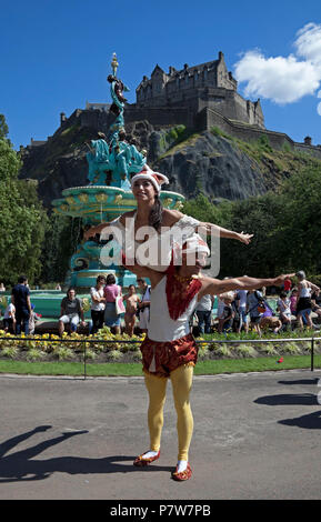 Edinburgh, Scotland, UK. 8 July 2018. Ross Fountain, West Princes Street Gardens switch on day, crowds of families and tourists flock in the sunshine to see the circus acts and Edinburgh School's pipe band and bathe in the fountain water which was switched off in 2010. Stock Photo