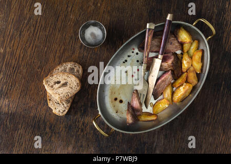 Top view beef steak with fried potatoes in frying pan on dark background. Dinner table concept Stock Photo