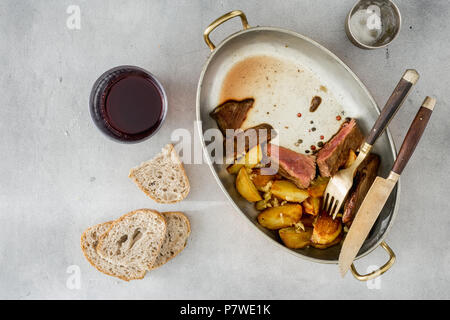 Top view slices of beef steak with potatoes in frying pan on light surface with glass of red wine Stock Photo