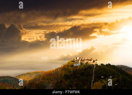 Rasnov medieval citadel in Transylvania in amazing sunset light surrounded by bright autumn-colored hills. Stock Photo