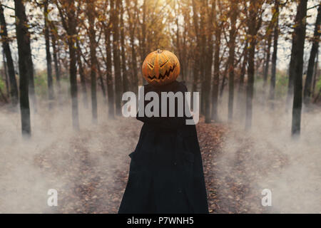 Portrait of a scary Jack-lantern with a pumpkin on his head. Halloween legend. Dressed in black coat. Autumn forest Stock Photo