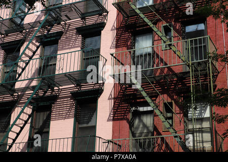 Close up of two old brick buildings in lower Manhattan painted pink and red, with green fire escapes that cast interesting shadows on their facades Stock Photo