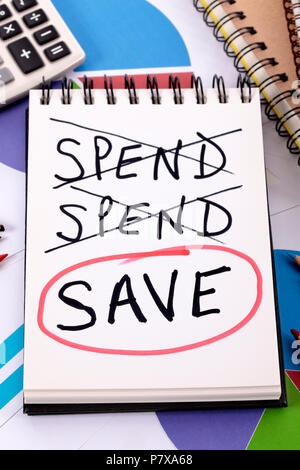 The word Save circled in red below a list of spending written on a notepad surrounded by pencils, graphs, books and calculator. Stock Photo