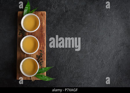 Green tea in ceramic cups, dry green oolong tea and tea leaves on black stone table, copy space. Stock Photo