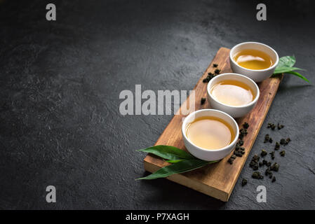 Green tea in ceramic cups, dry green oolong tea and tea leaves on black stone table, copy space. Stock Photo