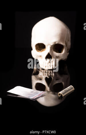 cocaine, Herion or other illegal drugs that are sniffed by means of a tube or injected with a syringe, money and Skull, isolated on black glossy backg Stock Photo
