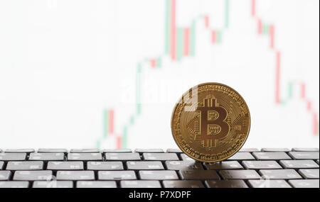 Golden bitcoin on the keyboard, in the background a white graph of growth and falling prices Stock Photo
