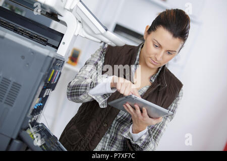 woman fixing printer while looking for answers in tablet Stock Photo
