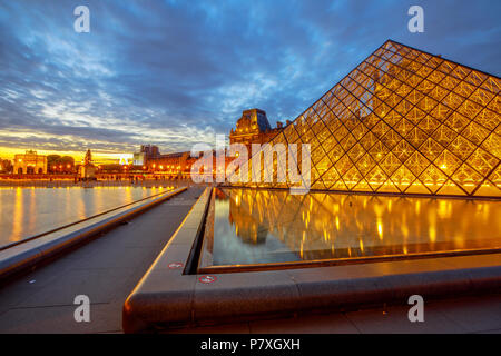 Paris, France - July 1, 2017: wide angle view of glass Pyramid and Pavillon Rishelieu reflecting at twilight. Cour Napoleon at blue hour. Cultural art picture gallery hosting Gioconda of Leonardo. Stock Photo