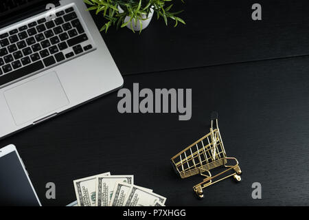 Gold cart, cash and gadgets on a black table. Stock Photo