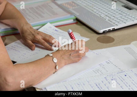 woman working from home, reviewing documents, correcting exams, with the pen in her hand Stock Photo