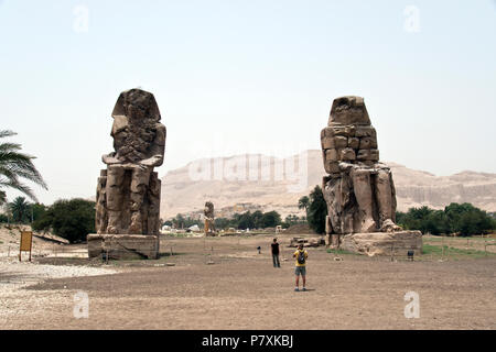 Tourists make photos at the Colossi of Memnon, two massive stone statues of Pharaoh Amenhotep III, at the Theban Necropolis, Luxor, Egypt. Stock Photo