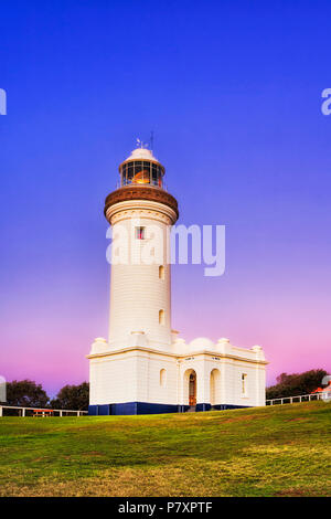 Pink blue sunrise over Norah Head lighthouse on Australian Central coast - top of the hill with green grass around historic landmark building. Stock Photo