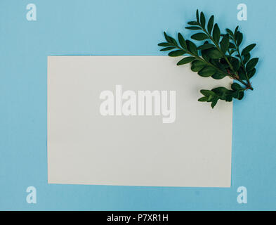 Desktop mock-up with blank paper card, branch on white shabby table background. Empty space. Styled stock photo, web banner. Flat lay, top view. Stock Photo