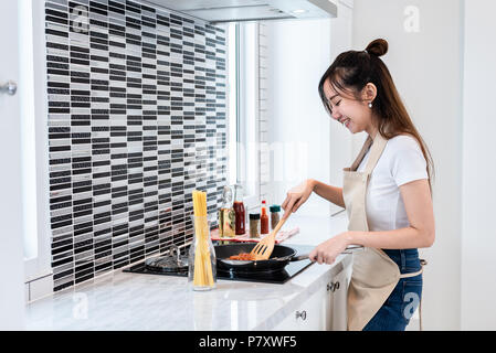 Asian woman cooking spaghetti in kitchen happily. People and lifestyles concept. Food and drink theme. Interior decoration and housework theme. Stock Photo