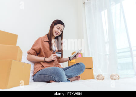Beauty Asian woman using tablet and credit card. Start up small business entrepreneur SME and checking order list in bedroom, Young happy freelance wo Stock Photo