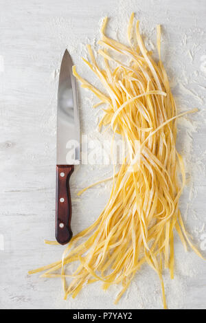 Raw homemade noodles with a large kitchen knife on a white background, top view Stock Photo