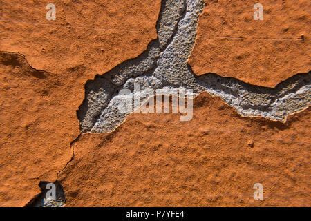 Orange peeling paint on a grey cracked concrete wall. Stock Photo