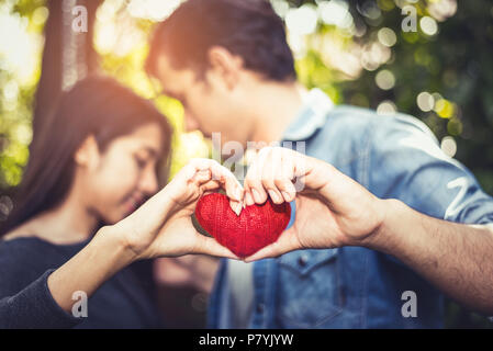 Two hands of young lovers or couple holding Red Heart yarn in middle at natural outdoor background for Valentines day. Holiday and relax concept. Hone Stock Photo