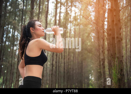 Asian beauty woman drinking water in forest. Sport and Healthy concept. Jogging and Running concept. Relax and take a break theme. Outdoors activity t Stock Photo