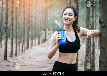 Asian beauty woman drinking water in forest. Sport and Healthy concept. Jogging and Running concept. Relax and take a break theme. Outdoors activity t Stock Photo