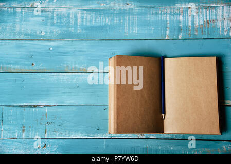 Top view of blank open notebook on blue wooden background with purple pencil in middle. Working stationery office. Education and Business concept. Min Stock Photo