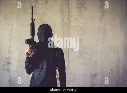 Terrorist holding rifle gun on grunge wall. Social issued theme. Terrorist and Robber concept. Police and Soldier theme. Social issued theme. Stock Photo