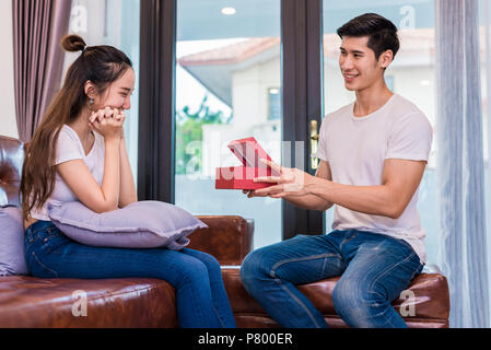 Boyfriend surprising girlfriend with present. Woman surprised when looking at gift box on special day. Lovers and Couples concept. Honeymoon and Datin Stock Photo