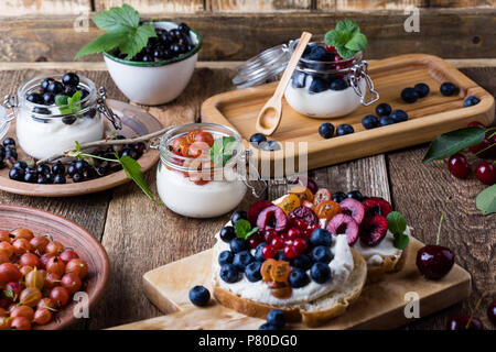 Cream cheese sandwiches and cheesecake creme parfait with fresh summer fruits in jar, healthy breakfast Stock Photo
