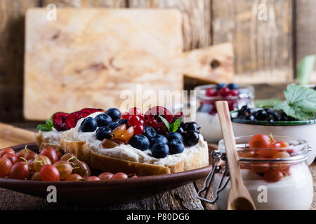 Cream cheese sandwiches and cheesecake creme parfait with fresh summer fruits in jar, healthy breakfast Stock Photo