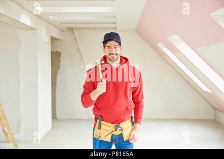 Portrait of happy young repairman holding hammer in his hand while standing at construction site. Stock Photo