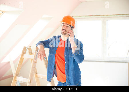 Handsome young repairman using his mobile phone while standing in the house and working on interior repairs. Stock Photo