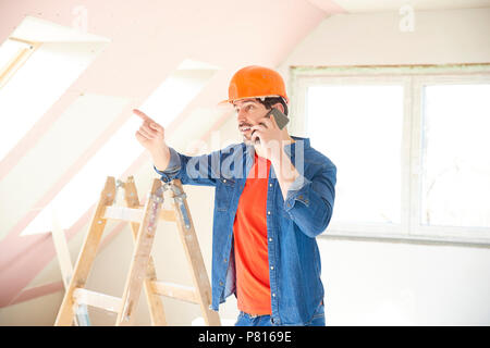 Handsome young repairman using his mobile phone while standing in the house and working on interior repairs. Stock Photo