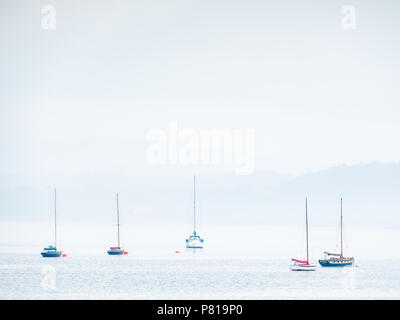 Five sailing boats moored at Beaumaris on the Isle of Anglesey in Wales on a calm and sunny day with mist rolling in Stock Photo