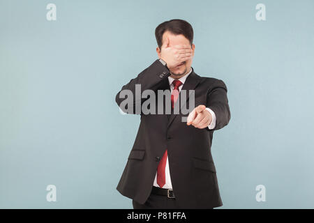 I do not want to see, is that a surprise? indoor studio shot. isolated on light blue background. handsome businessman with black suit, red tie and mus Stock Photo