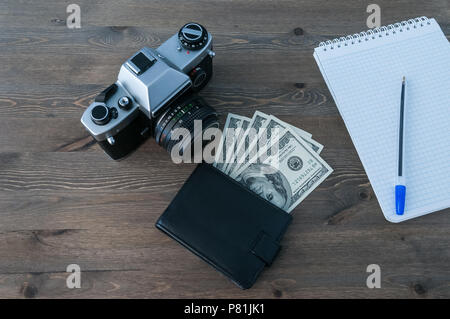 A retro camera, a purse with money and a notebook with a pen on a wooden table. Stock Photo