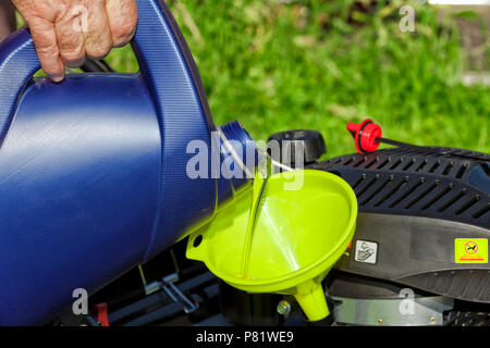 A man pours oil on his lawn mower using a funnel. Stock Photo