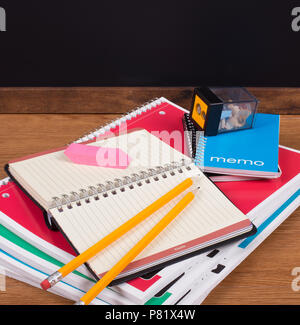Stack of school notebooks on a desktop with a blank blackboard in background Stock Photo