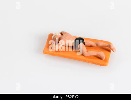 Miniature man in swimming costume lying sunbathing on a bright orange towel on the beach in a concept of a summer vacation isolated on white with copy Stock Photo