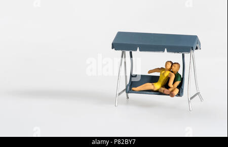 Loving miniature couple relaxing on a swing seat on the porch in a close embrace isolated on white with copy space Stock Photo