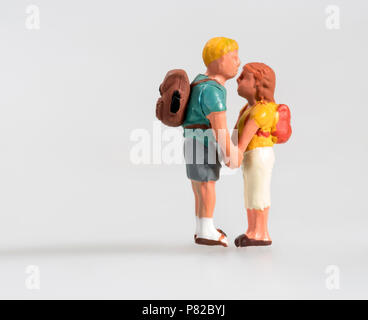 Miniature young couple in love wearing backpacks standing facing each other holding hands isolated on white with copy space in a show of affection Stock Photo
